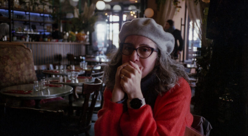 A photograph of a woman wearing a beret in a bar in Paris. Taken with a Canon F1New and Fujicolor Colorplus 400 film.