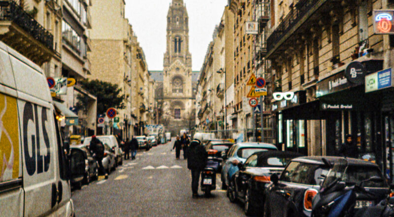 A photograph of a cathedral spire at the end of a narrow street in Paris. Taken with a Nikon L35AF using Fujicolor Colorplus 400 film.