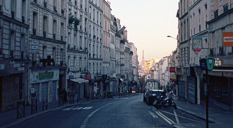 A photograph of the Eiffel Tower in the distance looking down a narrow street in Paris.