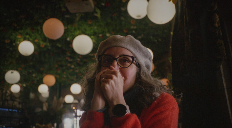 A woman covers her mouth while smiling and wearing a beret in a bar in Paris. Taken with a Nikon L35AF using Fujicolor Colorplus 400 film.
