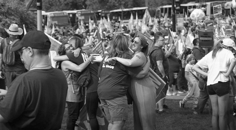 A photograph of protestors hugging from a union rally in support of Quebec service workers including teachers and nurses near the Sir George-Etienne Cartier Monument in Montreal during the summer of 2023. Taken with a Canon F1New using CatLabs 320 film.